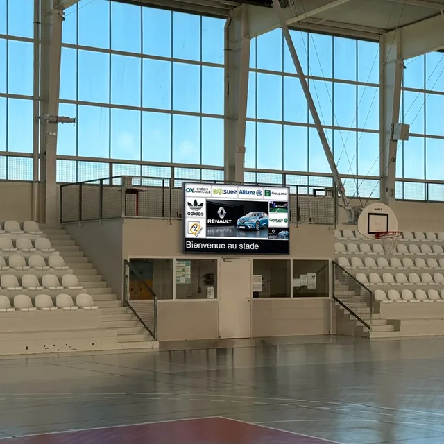 Écran LED dans un gymnase, avec un message de bienvenue et des sponsors.